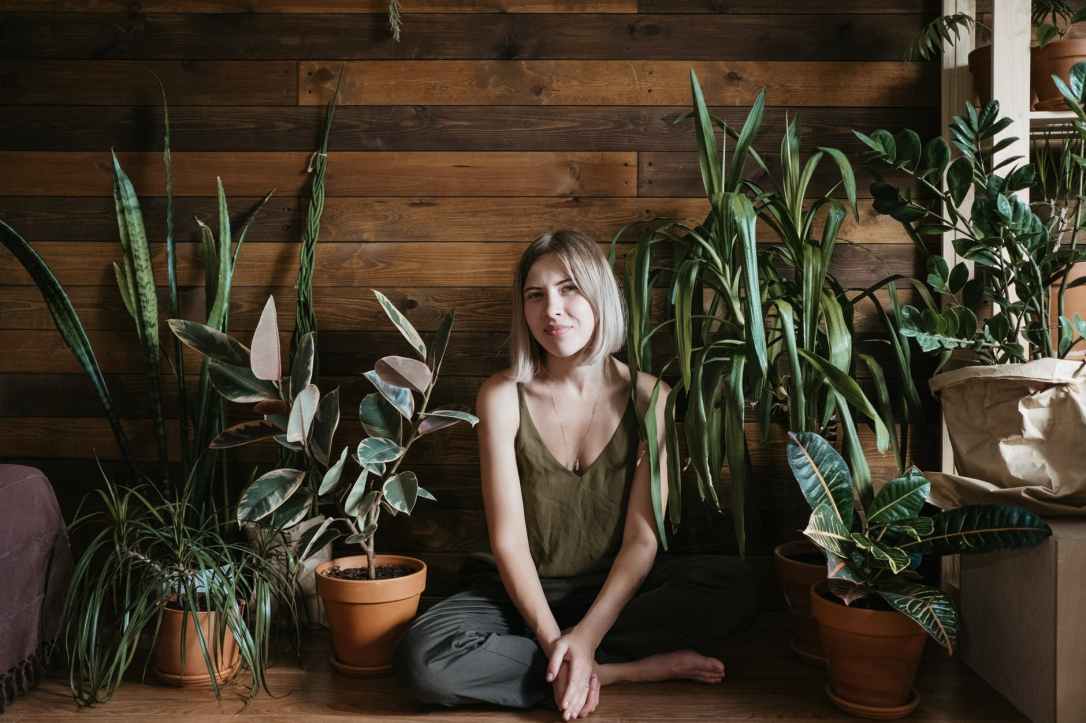 woman sits on the floor between indoor plants