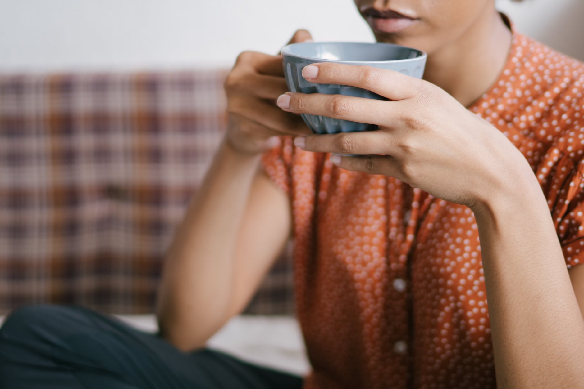 selective focus close up photo of woman in orange top holding gray cup